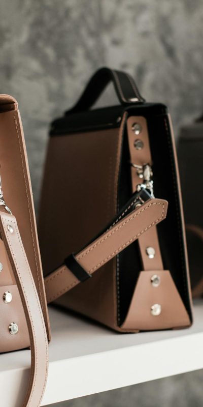 Luxury leather handbags displayed on a white shelf, showcasing minimalistic design and various colors.
