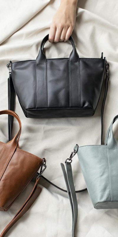 Top view of three stylish leather bags in black, brown, and gray on a soft fabric surface.