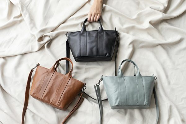 Top view of three stylish leather bags in black, brown, and gray on a soft fabric surface.